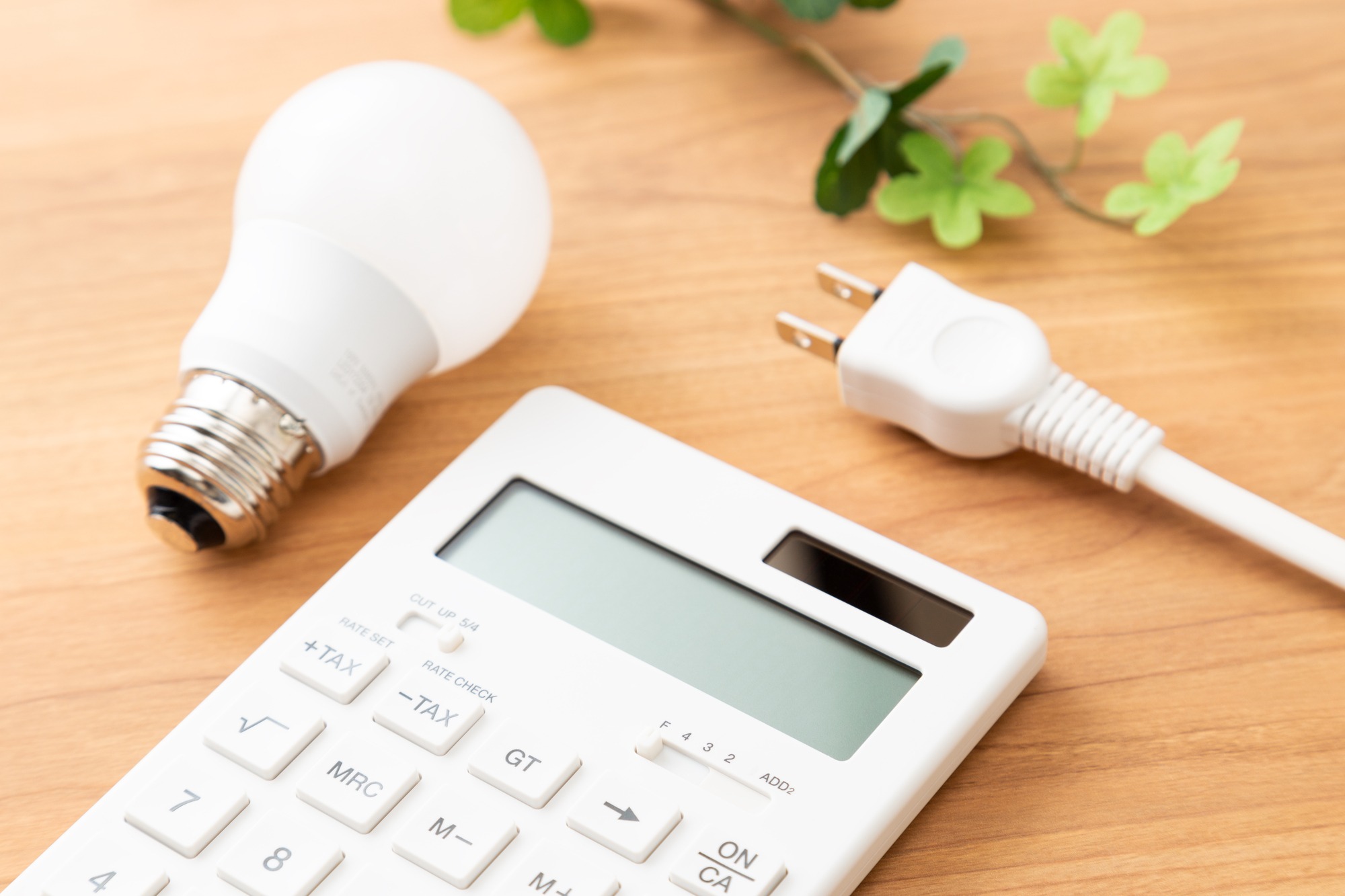 木のテーブルに置かれた電球と電卓とコンセントプラグ